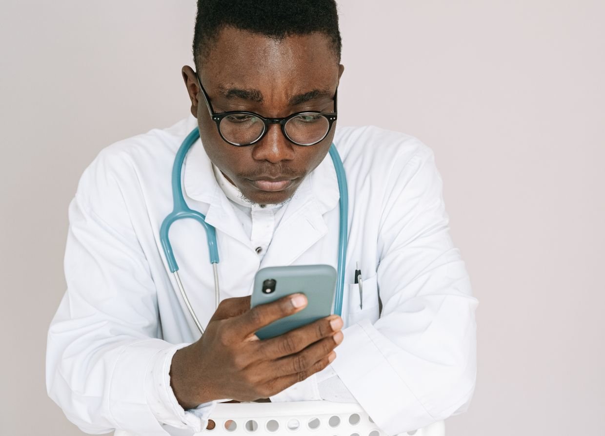 Médico de jaleco lendo atentamente a tela do celular